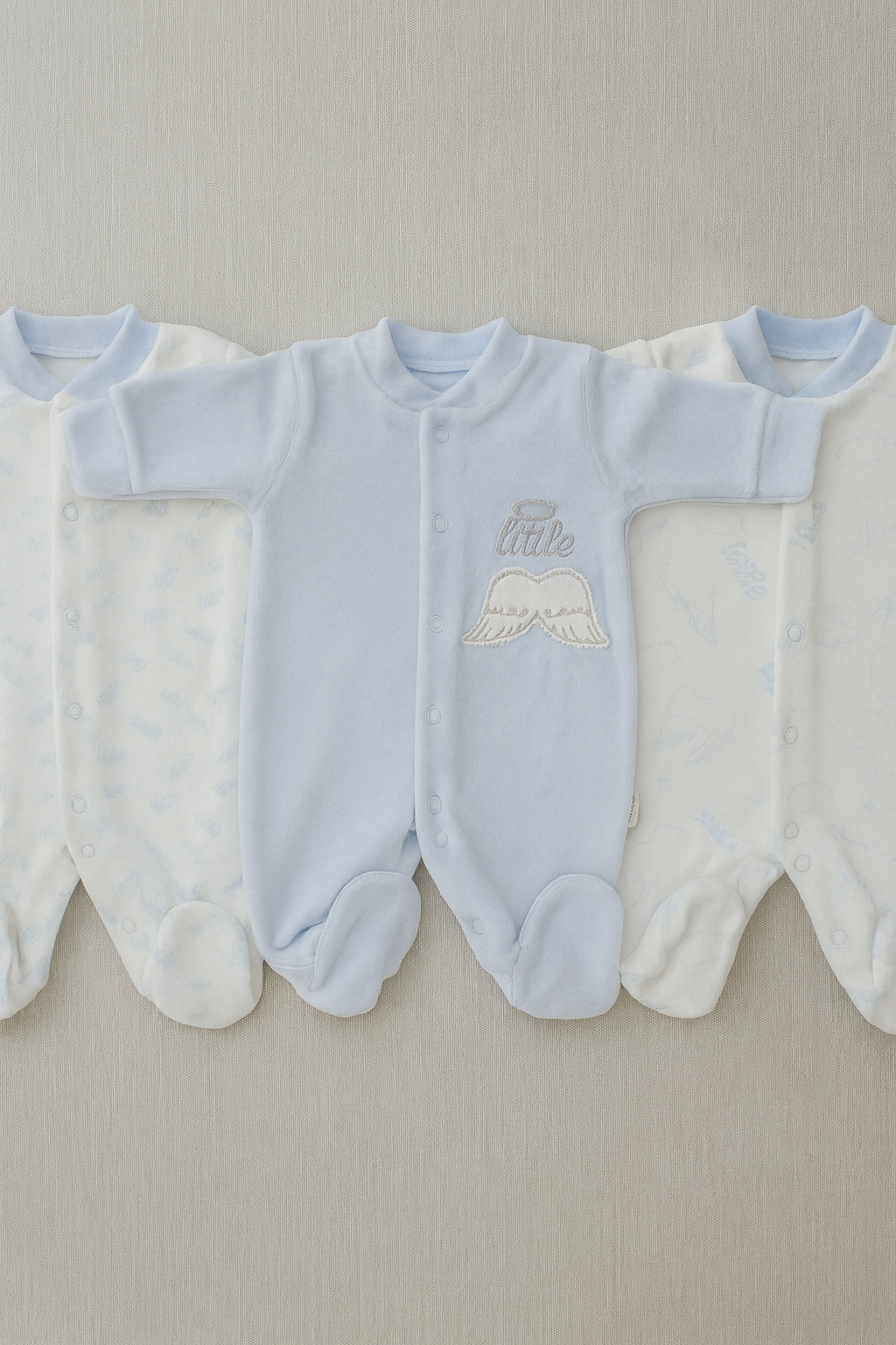 Three light blue baby rompers with embroidered text on a neutral background